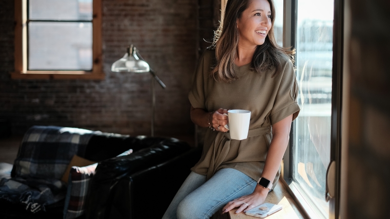 Young women gazing out of her loft window with coffee in hand - Quad Cities